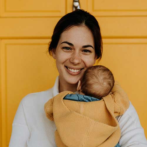 Na zdjęciu uśmiechnięta kobieta z niemowlęciem na ręku.