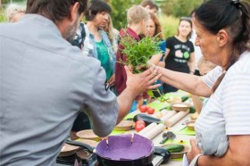 Na zdjęciu: Warsztaty kulinarne we Wspólnym Ogrodzie; grupa osób przy zastawionym naczyniami stole.  Fot. Dominika Dzieniszewska