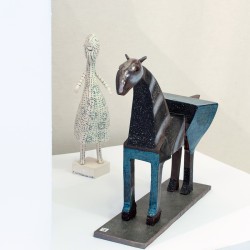 Ceramiczna rzeźba konia utrzymana w kolorach brązu i błękitu. Obok figurka kobieca w bieli. Powierzchnia rzeźby malowana w delikatne kwiatowe wzory.