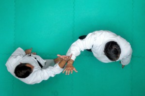 Zdjęcie przedstawia dwóch mężczyzn z perspektywy lotu ptaka. Obydwoje ubrani są w biały strój charakterystyczny dla japońskiej sztuki walki. 