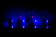Fotografia przedstawia grupę osób na scenie. Widoczne są ich same kontury. Na scenie przeważa niebieskie światło. 