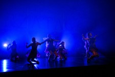 Zdjęcie przedstawia tancerki na scenie teatralnej w ciemnym, niebieskim świetle. 