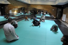 Na zdjęciu widoczna jest sala do ćwiczeń oraz siedzący na macie uczestnicy warsztatów podczas ćwiczeń. 