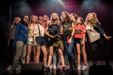 Spektakl "Hejt Made"  / Na zdjęciu widzimy grupę młodych dziewcząt kolorowo ubranych stojących na scenie teatralnej. 