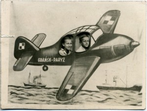 Dwóch chłopców (nastolatków) pozuje do zdjęcia z namalowanym samolotem z napisem "Gdańsk-Paryż". Dzieci pozują ustawione za dużym, wymalowanej płachcie z wyciętymi dziurami symulującymi szyby samolotu. Fotografia w odcieniach szarości i sepii.