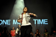 Zdjęcie przedstawia tancerkę tańca Hip-Hop na scenie podczas pokazów. W tle widać pozostałą część grupy.