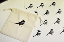 Na zdjęciu widoczne są prace: torba oraz materiał zadrukowane tym samym nadrukiem. Są to czarne ptaki. 