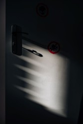 Na zdjęciu przedstawione są białe drzwi z dwoma rysunkami w kolorze czerwieni. Światło pada z lewej strony tworząc cień z klamki. Fot. Agnieszka Mocarska