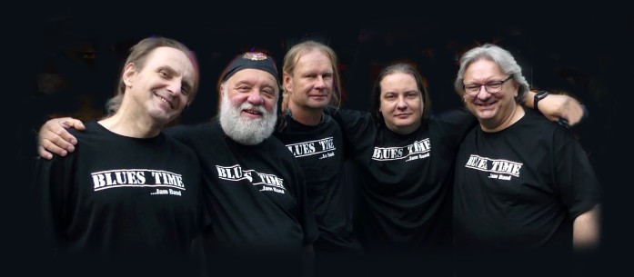 Na zdjęciu grupa uśmiechniętych i obejmujących się w przyjacielskim objęciu pięciu mężczyzn - członków zespołu - ubranych w czarne koszulki z napisem zespołu "Blues Time", 
