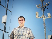 Na zdjęciu: Marcin Popkiewicz obok urządzeń pomiarowych na tle bezchmurnego nieba