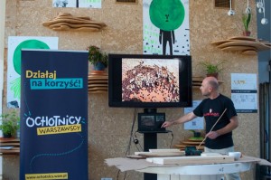 Zdjęcie przedstawia mężczyznę prowadzącego wykład na temat pszczół. W tle znajduje się roll-up programu Ochotników Warszawskich.
