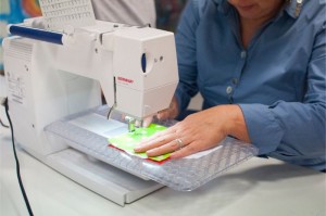 Zdjęcie przedstawia maszynę do szycia oraz dłonie szyjącej kobiety.