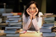 Na zdjęciu: Marta Abramowicz przy stole między stertami książek; opiera głowę na dłoniach.