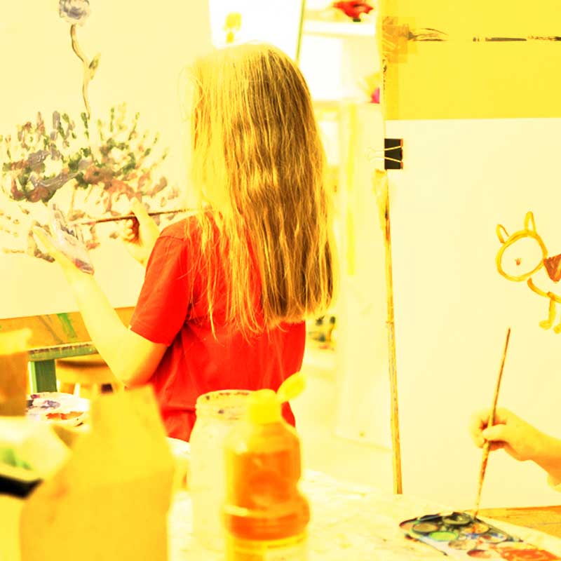 Zdjęcie: zbliżenie na dziecięce dłonie trzymające dwa pędzle i malujące obrazek. 